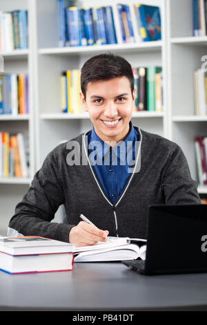 Happy student is learning in library. He is using laptop. Stock Photo