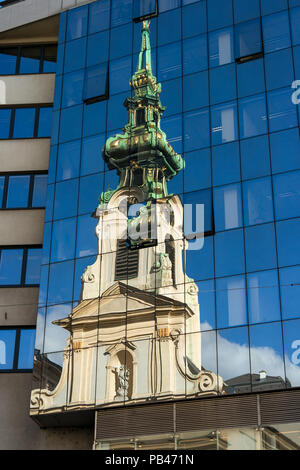 An old detailed Vienna church tower with copper roof reflects in the glass mirrored windows of a modern office tower. Vienna, Austria. Stock Photo