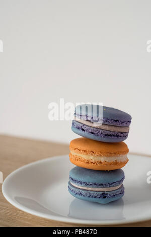 Leaning Macaron Tower in Blue and Orange Sitting on a Plate on a Wooden Counter in Front of a Light Colored Background Ready for Text Stock Photo