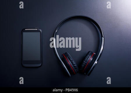 Black Mobile Phone Lying Next A Black Overhead Headset On Dark Background With Reflection Stock Photo