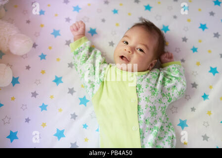 Curios little baby girl laying on bed and look in camera Stock Photo