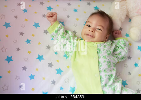 Happy baby girl laying on bed with hands up Stock Photo