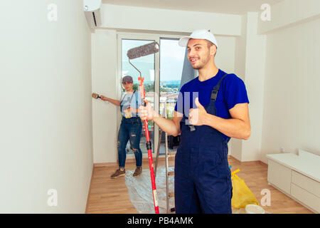Couple decorating room using paint rollers and paintbrush on wall Stock Photo