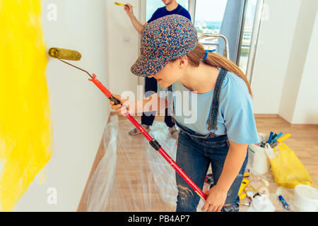 Couple decorating room using paint rollers and paintbrush on wall Stock Photo