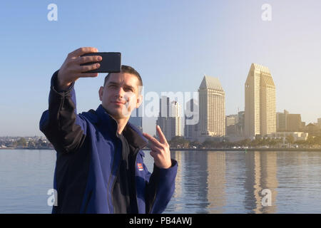 Cheerful happy man making peace gesture on selfie on background San Diego downtown. Selfie shooting on phone in background of San Diego, California, U Stock Photo