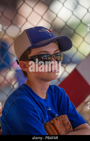 12 Year old boy, holding glove, looking thoughtfull, close up, wearing hat, blue jersey and red shoes, sunglasses. Model Relese #105 Stock Photo