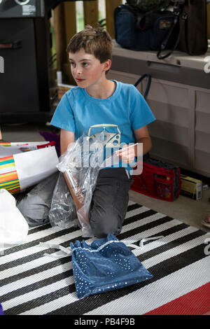 Blue t-shirt wearing birthday boy, on his knees, opening his presents. Model Release #105 Stock Photo