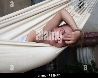 Portrait of a usually very pretty young 20 year old girl relaxing on a hammock pulling a silly funny face for camera Stock Photo