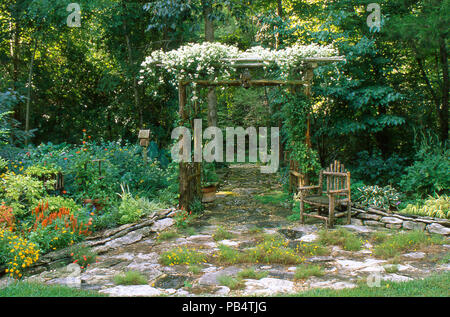 Blooming clematis on rustic handbuilt cedar arch with stone patio in a shaded area in a rock garden, Missouri USA Stock Photo