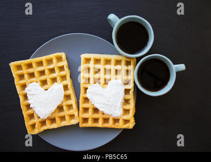 Delicious Belgian waffles with cream on a black background and two cups of coffee. Stock Photo