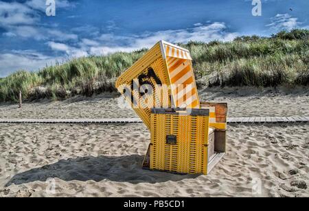 gelber Strandkorb vor den Dünen Stock Photo