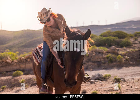 cheerful red hair lady ride a beautiful brown horse in friendship and enjoy the outdoor day together. relationship and pet therapy. happy and joy life Stock Photo