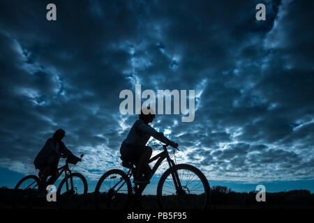 couple of rider in mountain bike come back home after a sport bikes session outdoor. beautiful blue sky with clouds in backgorund. people in silhouett Stock Photo