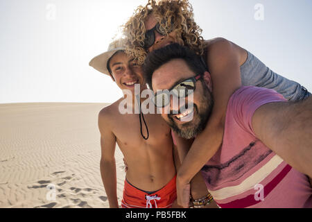 happy family taking selfie picture on vacation during the summer holiday at the beach. fuerteventura desert and three caucasian people having fun and  Stock Photo