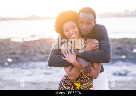 happy beautiful black race african couple in love or friendship stay together walking hugged with big smilies under the sunlight of the summer in vaca Stock Photo