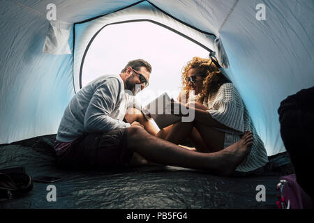happy young middle age couple married and in relationship enjoy the camping inside the tent and use tablet internet technology. love and friendship fo Stock Photo