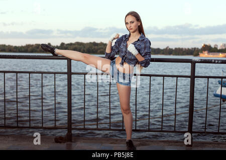 Young woman fighter doing sports stretching on the river bank. Stock Photo