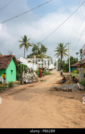 Naralapura, Karnataka, India - November 1, 2013: View on main brown dirt road on village with a few houses, women with children in front of them. Gree Stock Photo