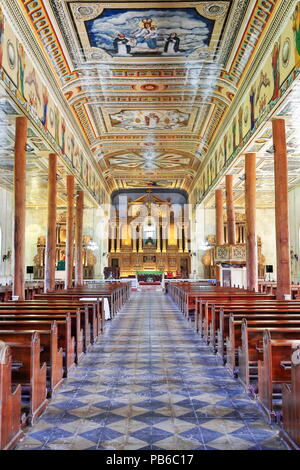 Pillars made of large tree trunks mark the nave and hold the tin ceiling painted with religious scenes in the trompe-l'oeil style. Santa Monica Parish Stock Photo