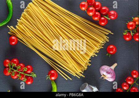 Uncooked pasta spaghetti on black background, red cherry tomatoes and garlic for sauce, top view Stock Photo