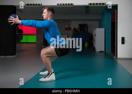 Handsome Young Man Doing Squad With Medicine Ball As Part Of Bodybuilding Training Stock Photo