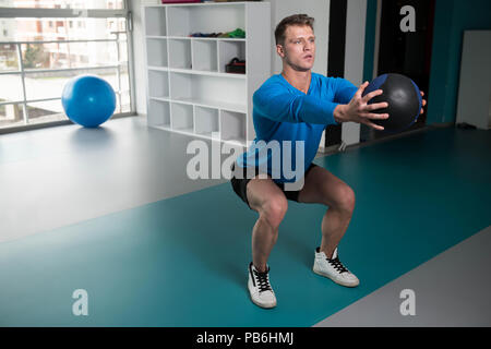 Handsome Young Man Doing Squad With Medicine Ball As Part Of Bodybuilding Training Stock Photo