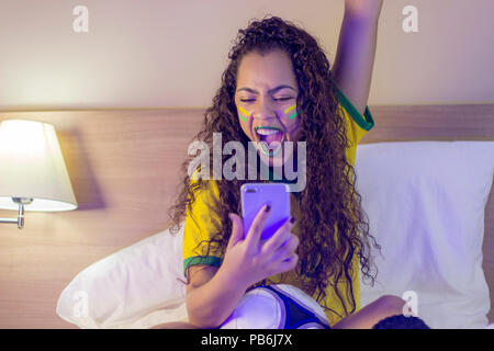 Supporter of the Brazilian football team celebrating a goal by watching the smartphone Stock Photo