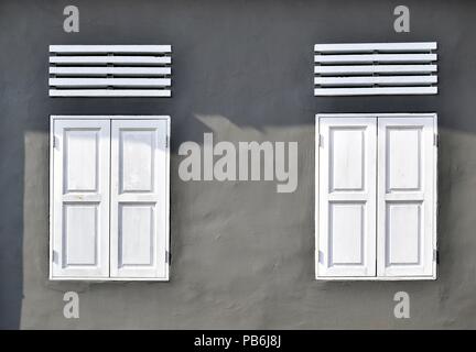 Front view view of white antique windows with wooden shutters on the gray wall of a house in Singapore as vintage background with space for copy. Stock Photo