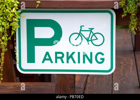 Bicycle parking sign on a wood fence with plants growing around it. Stock Photo
