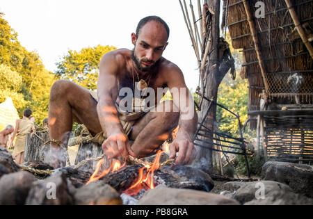 Albersdorf, Germany. 24th July, 2018. A man lights a fire next to a Stone Age hut. Around 80 men, women and children met in Alberdorf in the district of Dithmarschen under the motto 'largest Stone Age meeting since the Stone Age'. Credit: Axel Heimken/dpa/Alamy Live News Stock Photo