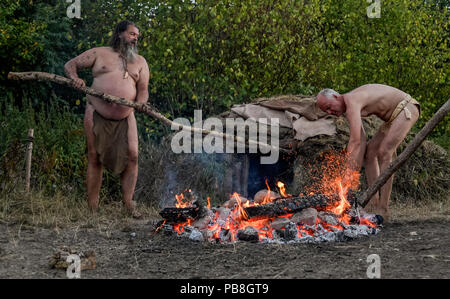 Albersdorf, Germany. 24th July, 2018. Two men heat up stones for a sauna they built themselves. Around 80 men, women and children met in Alberdorf in the district of Dithmarschen under the motto 'largest Stone Age meeting since the Stone Age'. Credit: Axel Heimken/dpa/Alamy Live News Stock Photo