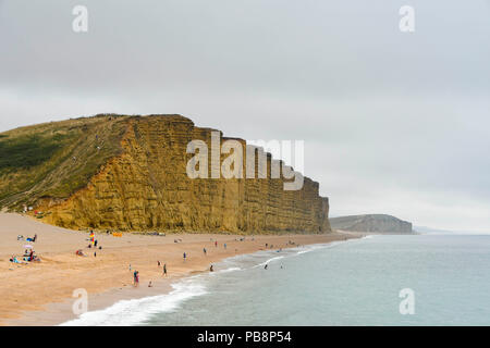 West Bay, Dorset, UK.  27th June 2018. UK Weather.  The beach is quieter on an overcast day at the seaside resort of West Bay in Dorset as temperatures drop as the heatwave ends.  Picture Credit: Graham Hunt/Alamy Live News Stock Photo