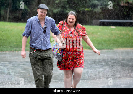 London, UK.  27 July 2018. UK Weather - A couple gets caught in a sudden heavy downpour outside Tate Modern.  Rain has finally arrived in the capital after weeks of dry weather during the current heatwave. Credit: Stephen Chung / Alamy Live News Stock Photo