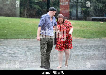 London, UK.  27 July 2018. UK Weather - A couple gets caught in a sudden heavy downpour outside Tate Modern.  Rain has finally arrived in the capital after weeks of dry weather during the current heatwave. Credit: Stephen Chung / Alamy Live News Stock Photo