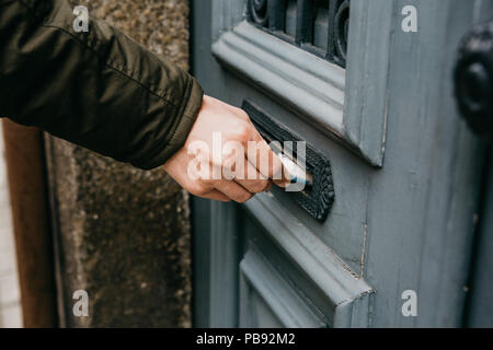 The postman puts a letter or newspaper or magazine in the mailbox at the door of a residential building or a person puts a brochure with advertising. Close-up. Stock Photo