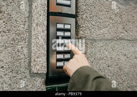 Close up the female hand presses the doorphone button. The girl is calling the intercom. Means of communication or notification of arrival and security of the entrance inside. Stock Photo