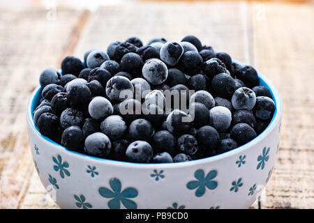 White bowl full with frozen aronia berries on wooden rustic table