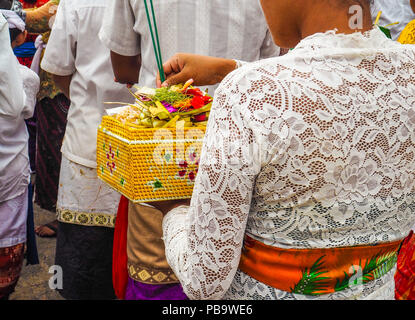 Young asian woman dressed in traditional clothing and waiting in line putting incense sticks in an offering basket she is holding for Balinese new yea Stock Photo