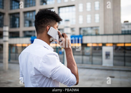 Young handsome Afro American man standing in front of huge modern business building; smiling and talking on mobile phone.