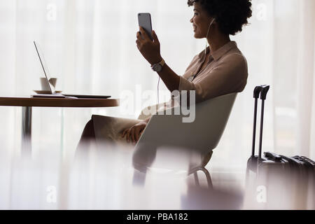 Happy woman making video call from mobile phone while sitting at airport lounge. Business woman waiting for flight at airport and using smart phone. Stock Photo