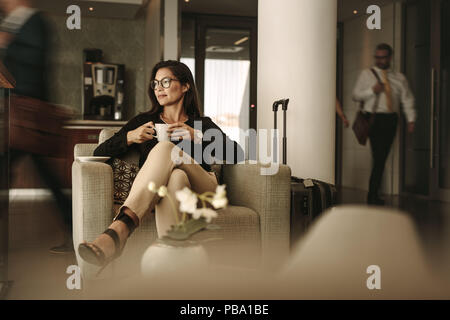 Businesswoman sitting at the airport lounge, waiting for the flight. Thoughtful woman sitting on sofa with coffee at airport waiting area. Stock Photo