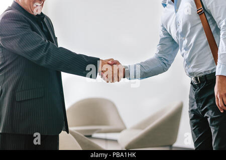 Two business men shaking hands in office. Senior businessman greeting and welcoming a young executive in office lobby. Stock Photo