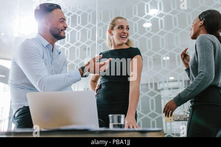 Multiracial business team discussing work and smiling in meeting room. Group of three happy office colleagues talking in boardroom. Stock Photo