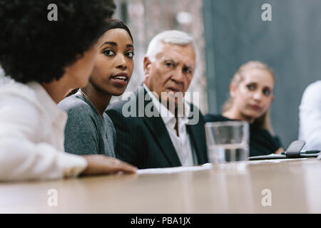 Business team sitting around a table and discussing new working plan. Focus on young african woman putting forward her ideas to team in meeting. Stock Photo