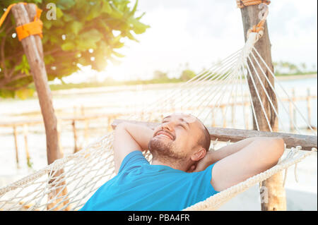 Time for laziness. The man lies in a hammock and enjoys the rest. Stock Photo