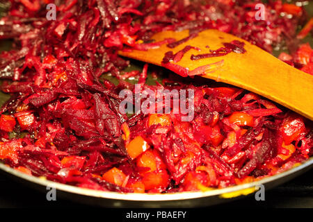 Finely chopped beets and carrots fried in a frying pan in oil. Mixing with a wooden spatula. The process of cooking vegetables for borsch or vegetable Stock Photo