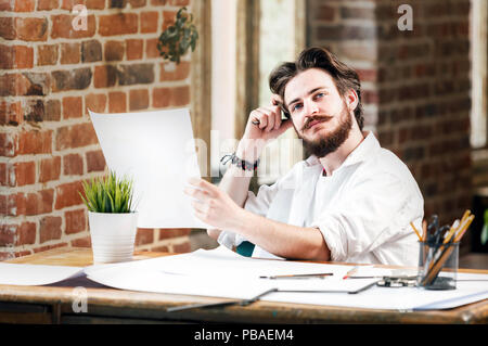 Bearded hipster male architect in white shirt with dividers looking on the blueprint in loft office Stock Photo