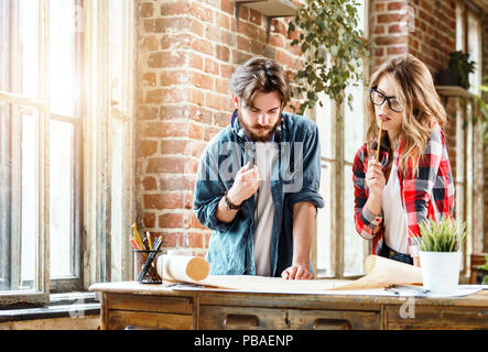 Team of young ambitious architects discussing plan on blueprint at the meeting in a loft sunny office Stock Photo