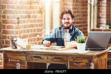 Handsome bearded male architect working on a building plan at his desk smiling to the camera joyfully copyspace professionalism trustworthy qualified experienced engineer constructionist developer Stock Photo