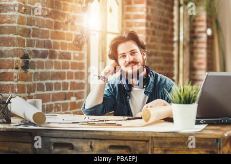 Handsome young bearded male architect smiling cheerfully sitting at his desk at the office copyspace, working drawing, designing, engineering, architectural creativity professional success worker businessperson Stock Photo